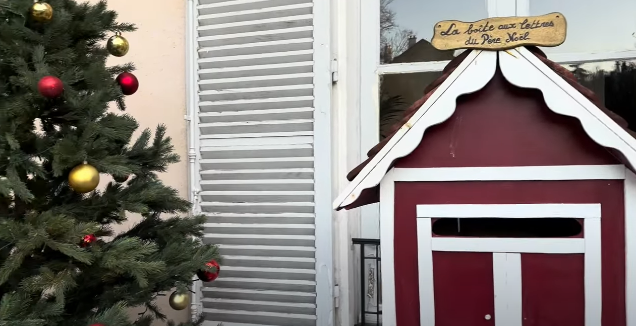 Un sapin de Noël est à gauche avec des boules rouges et jaunes. A droite il y a la boîte aux lettres du Père Noël